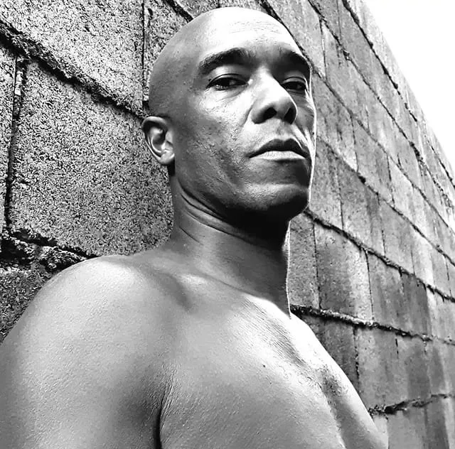 Black-and-white portrait of Marcus Chocollate leaning on a block wall.